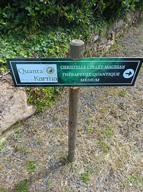 Un panneau indicateur vert émeraude avec le logo de l’entreprise Quanta Karma et le nom de la thérapeute Christelle Collet-Maussan